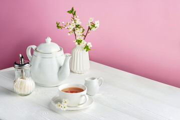 Tea set and cherry flowers on a pink background with copy space.