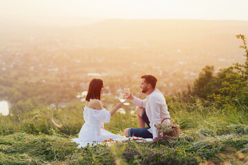 
Happy young couple having romantic picnic in mountains and clinking glasses with white wine.