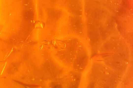 Texture of transparent yellow gel with air bubbles and waves on orange background. Concept of skin moisturizing, body care and prevention of covid19. Liquid beauty product closeup. Backdrop, flat lay