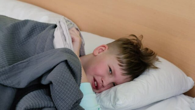 A sad boy is lying on the bed with a fever and a headache, and he has a headache. The face is distorted with pain. Takes out the thermometer. High quality 4k footage
