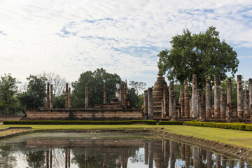 Ancient Buddha statue and ruin of temple in Wat mahathat temple with reflection on a pond in Sukhothai Historical Park, which also one of UNESCO Heritage Site
