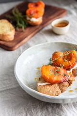 Summer Breakfast - toast (sandwich, bruschetta) with grilled peaches, cream cheese (ricotta, mascarpone), thyme and honey on beige linen tablecloth. Selective focus