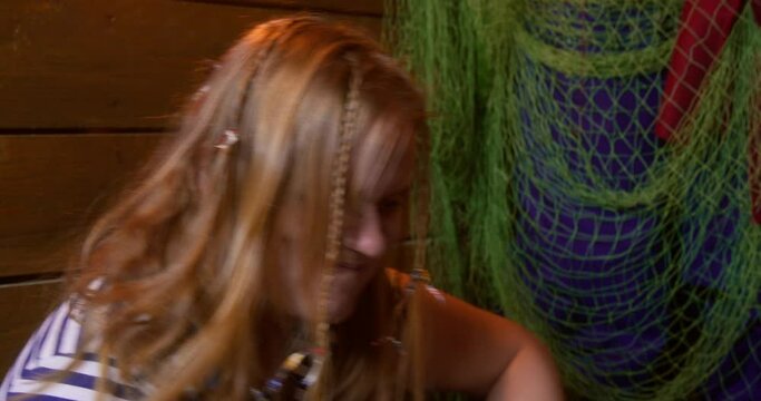 Pirate gives flick to sloppy woman with braids in striped sailor shirt playing craps INwooden cabin against green mesh closeup