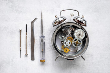 Watch mechanism and watchmaker tools near open alarm clock