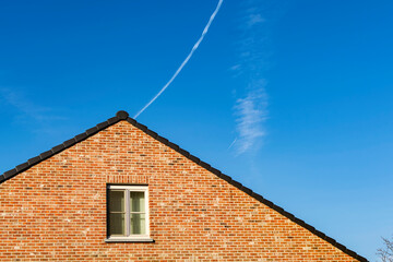 Gabled roof old brick house in Gavere town With jet smoke trail in the background sky. Gavere is located in the Belgian province of east flanders, Belgium