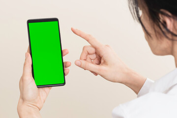 Woman using smartphone with blank green screen chromakey background. Rear view