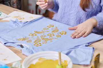 Women's hands fill the pattern on the fabric with paint.