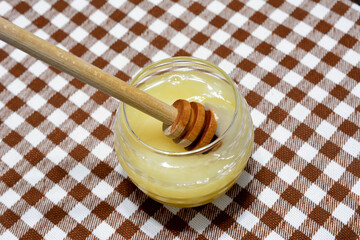 honey in jar with honey teaspoon on brown plaid tablecloth, close-up