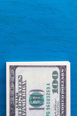 Vertical photo of a stack of hundred-dollar bills on a blue background with copy space. A wad of...