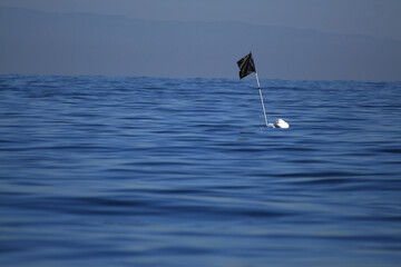 Bandiera nera realizzata con un sacco della spazzatura, in mezzo al mare, per indicare la posizione di una boa e palamito sott'acqua