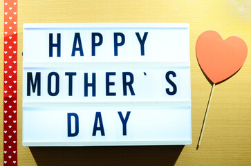a greeting message for Mother's Day: "happy mother's day" with the light box and a red heart on a wooden table.