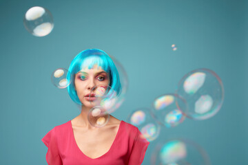 Beautiful young woman with blue wig and bright make-up in soap bubbles. Fashion model girl with creative color makeup. Women doll concept.