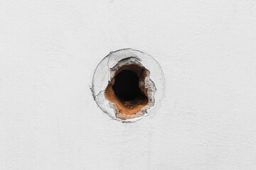 Hole in white concrete wall, cement surface damaged by round broken background hole