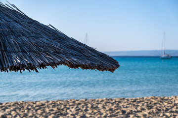 Straw umbrella closeup, blur sandy beach. Sunny day at sea. Summer holiday in Greece