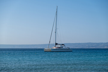 Sailing boat catamaran anchored at rippled sea, Land and blue sky background
