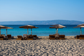 Summer holiday at seaside. Straw umbrella lounger in row on sandy empty beach sunny day.