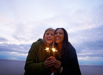 Celebrating the start of an awesome holiday. Two young women holding sparklers with the ocean and twilight sky behind them.