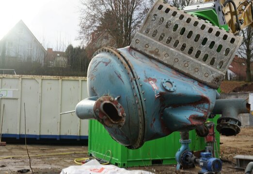 Baggerzange aus Stahl fasst alten blauen Filtertank aus Metall auf Baustelle im Winter