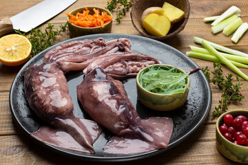 Raw squid with tentacles and bowl of seaweed on black plate.