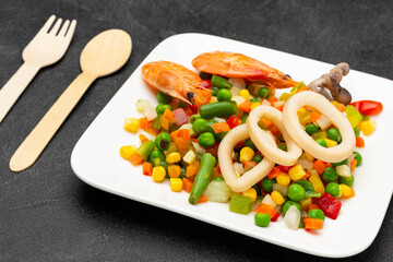 Shrimp and squid rings with mixed vegetables on white plate.