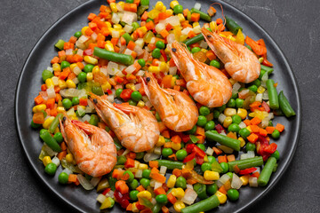 Shrimp with mixed vegetables and green asparagus on black plate.