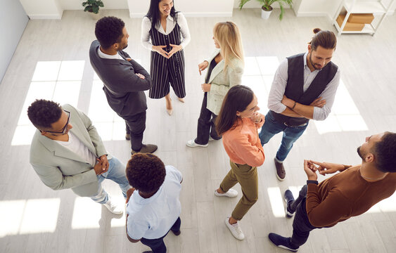 Group of diverse people communicating at business event. Smiling multi ethnic employees talking while standing in office at casual meeting or psychological training session. High angle shot from above