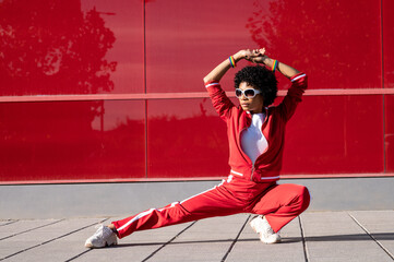 Young African American woman with short hair and sportswear practicing martial art over red colored wall on a sunny day