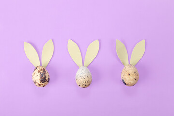Quail eggs with rabbit ears on a lilac background. minimalistic easter background