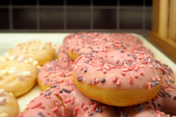a lot of round donuts in pink glaze with multicolored sprinkles are on a tray in the supermarket. bakery. side view