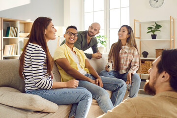 Happy multiethnic friends sit on couch gather at home have fun chatting talking together. Smiling...