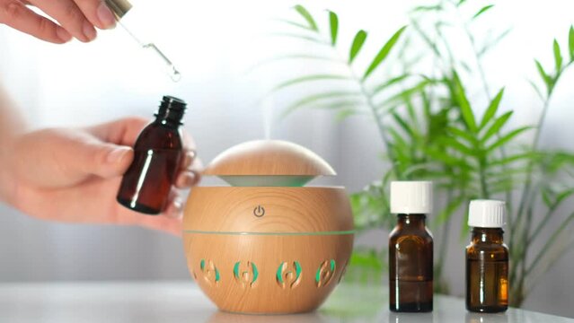 Modern aroma oil diffuser on the white table. Spa concept for body and health care. female is adding essential oil to an aroma diffuser.