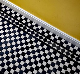 Black and white tiled geometric chequered Victorian floor below yellow wall