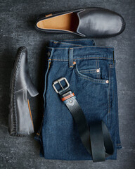 Flat lay mens jeans, moccasins and leather belt, mens fashion, top view, dark gray background