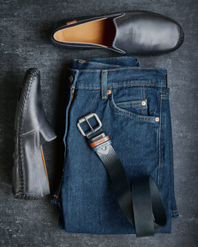 Flat lay mens jeans, moccasins and leather belt, mens fashion, top view, dark gray background