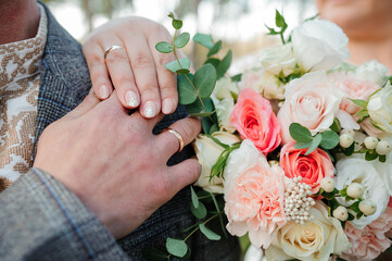 Golden wedding rings, hands of the bride and groom on a bouquet of flowers