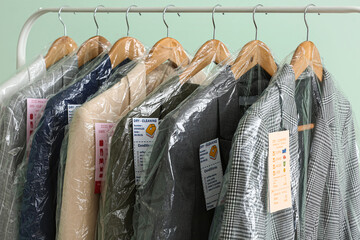 Rack with clean jackets in plastic bags on green background, closeup