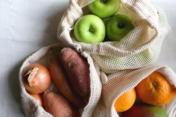 Reusable mesh bags filled with various healthy fruit and vegetable. Top view.
