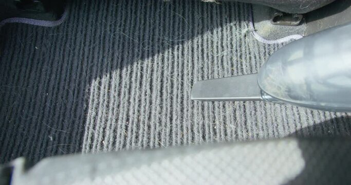 Person unsuccessfully tries to vacuum every crevice in dusty fabric car mat covered with fur and hair, using vacuum cleaner with special nozzle, close up. Dry cleaning of car interior.