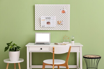 Modern workplace with different supplies and peg board on green wall
