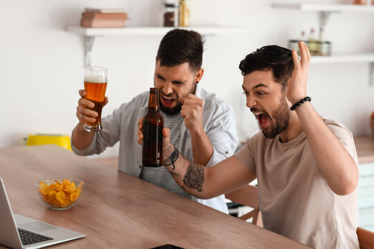 Happy Male Friends With Beer Watching Sport Game In Kitchen