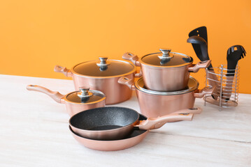Set of copper kitchen utensils on white wooden table against orange background