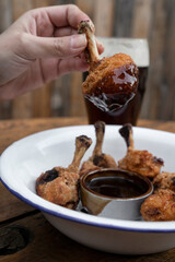 Eating. Closeup view of a hand holding a fried chicken wing dipped in bittersweet sauce.