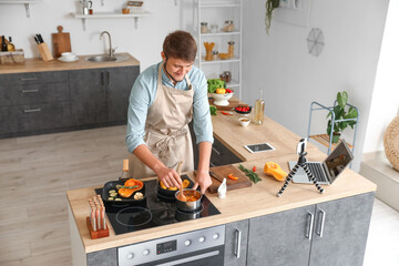 Young man cooking tasty vegetables while recording video tutorial in kitchen