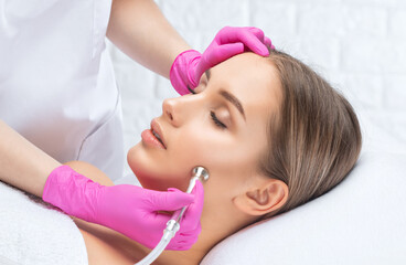 Obraz na płótnie Canvas Cosmetologist makes procedure microdermabrasion on the face against acne and blackheads near the eyes. Women's cosmetology in the beauty salon.