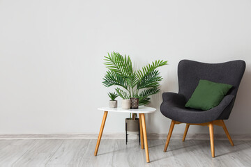 Modern armchair with table and plants near light wall