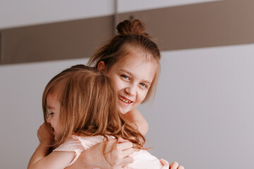 Two happy little girls hugging at cozy home. Big sister nursing her younger one.