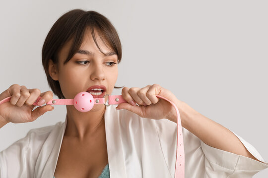 Beautiful young woman with mouth gag on grey background