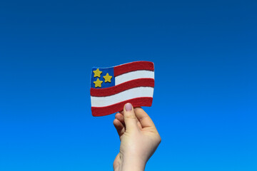 A hand holding USA small symbolic flag in front of clear blue sky. Idea for USA study, travel, election