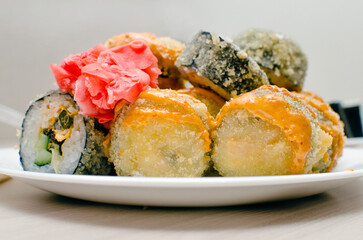 Fried rolls lie on a plate with red ginger leaves. Close-up, selective focus.