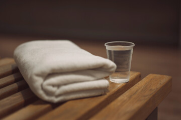 wooden bench in the gym with a white clean towel and a plastic cup of water and a blurred background